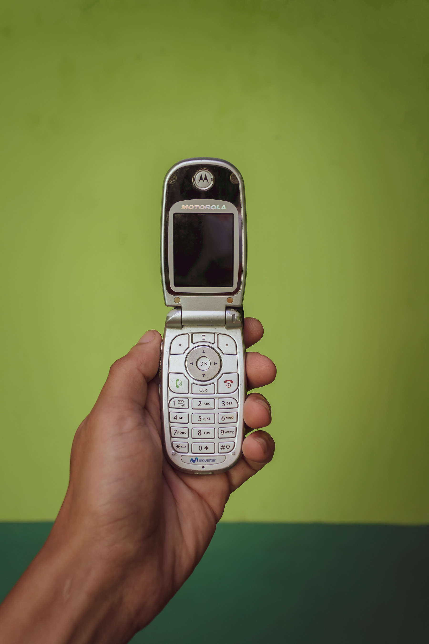 A hand holding an open flip phone, the keypad and small screen facing up.